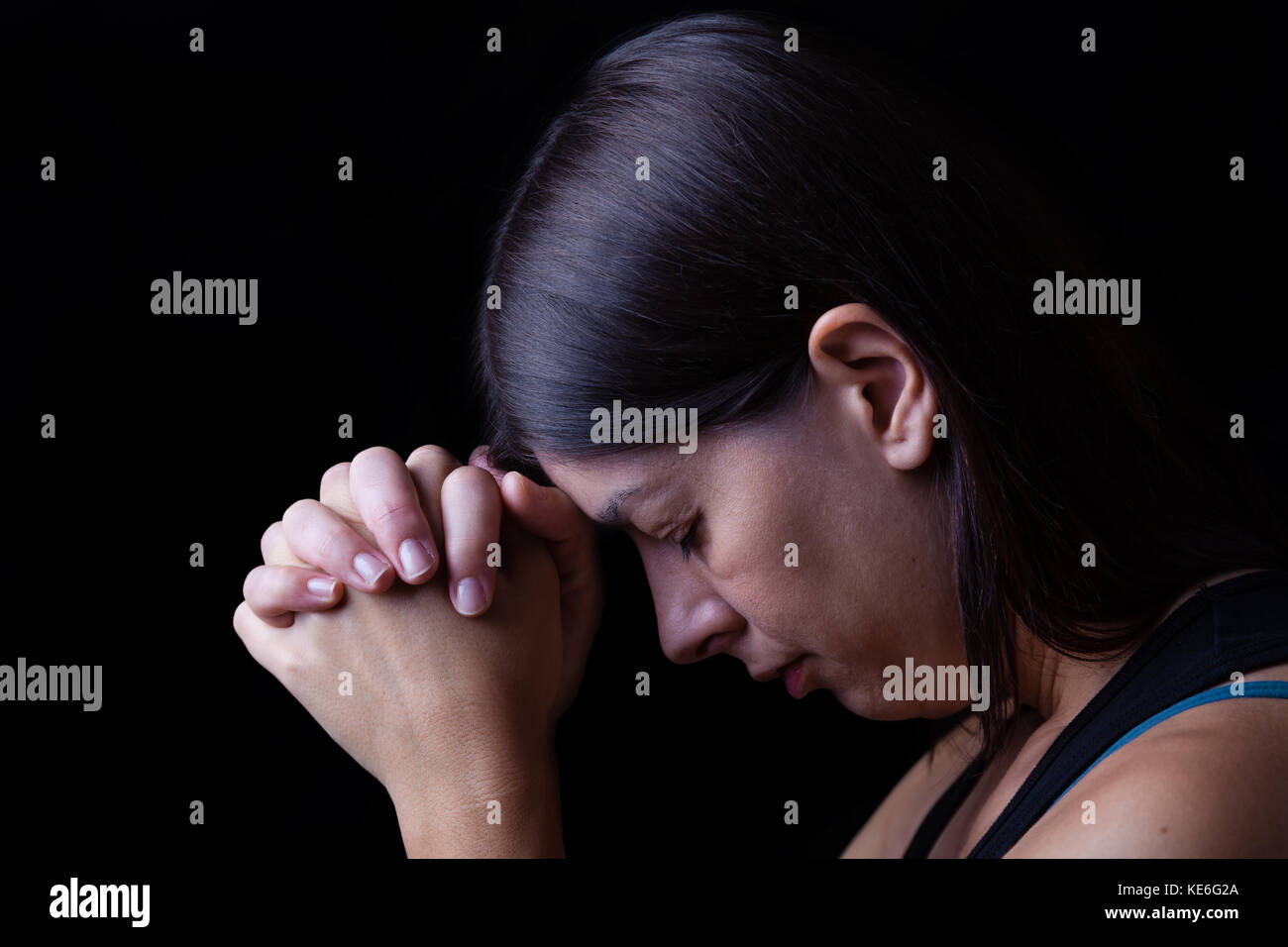 Treue Frau beten, Hände in der Anbetung zu Gott gefaltet, Kopf nach unten, die Augen geschlossen, in religiöser Inbrunst. schwarzer Hintergrund Gebet treu Hände gefaltet Stockfoto