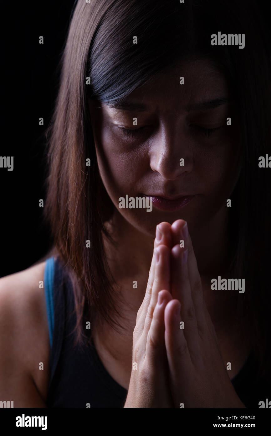 Gläubigen athletische Frau beten, Hände in der Anbetung zu Gott gefaltet, Kopf und Augen in religiöser Inbrunst geschlossen. schwarzer Hintergrund. Gebet portrait Stockfoto