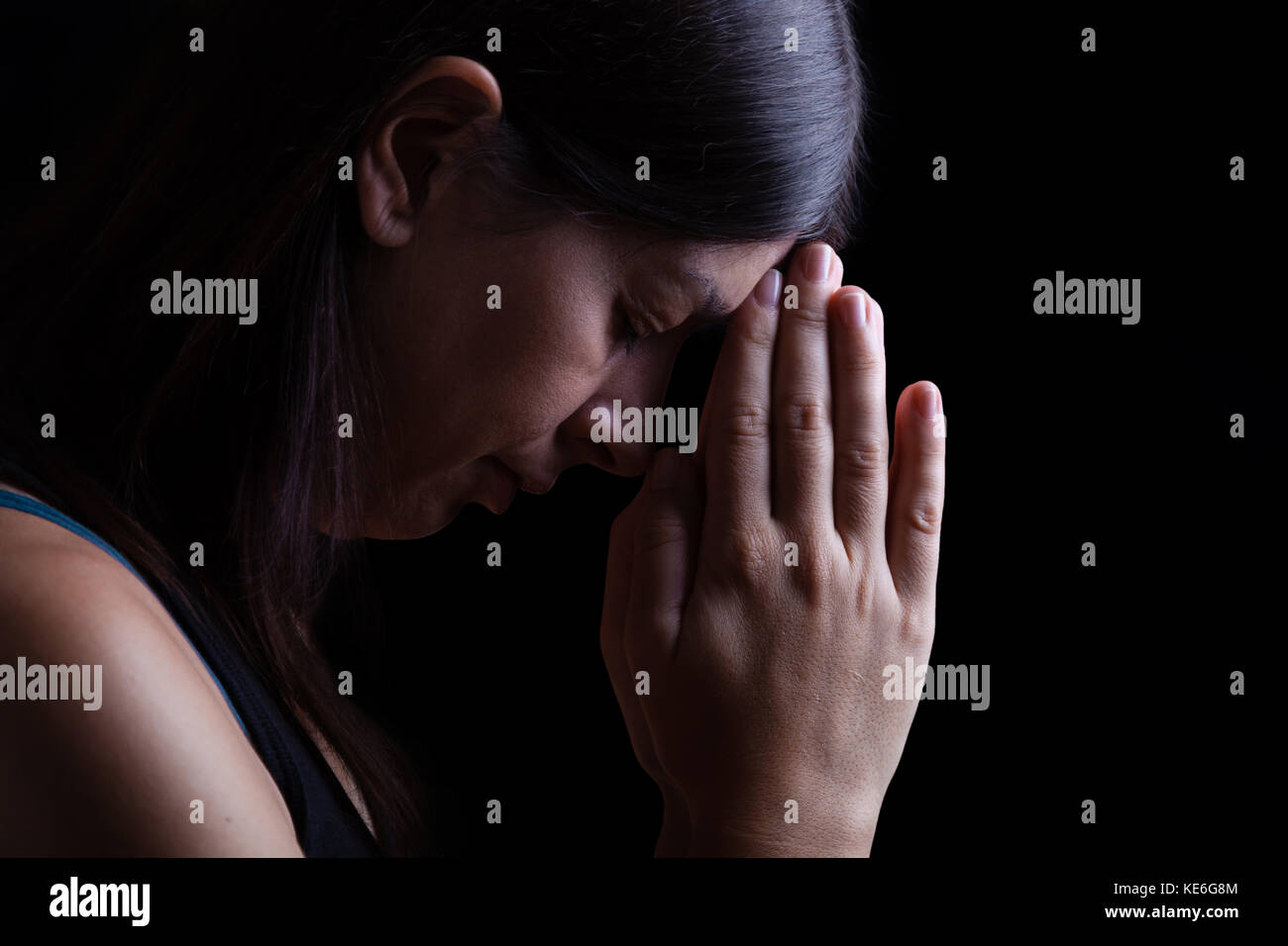 Treue Frau zu beten, die Hände gefaltet in der Anbetung mit Kopf nach unten zu Gott und Augen in religiöser Inbrunst geschlossen, auf einem schwarzen Hintergrund/Gebet portrait Stockfoto