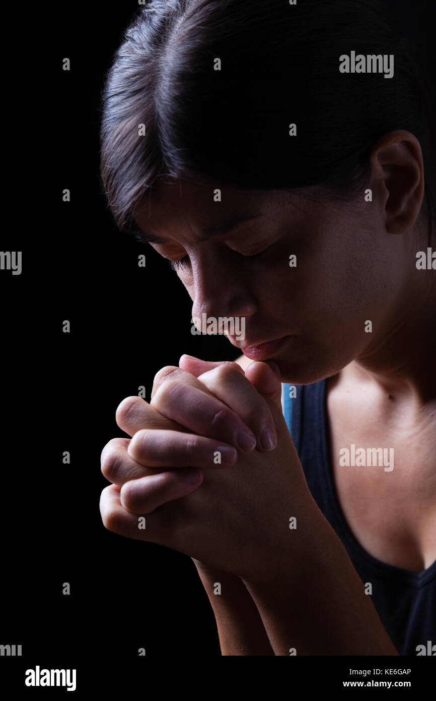 Low Key Porträt einer gläubigen Frau zu beten, die Hände gefaltet in Gottesdienst, Kopf und Augen in religiöser Inbrunst geschlossen, auf einem schwarzen Hintergrund. Stockfoto