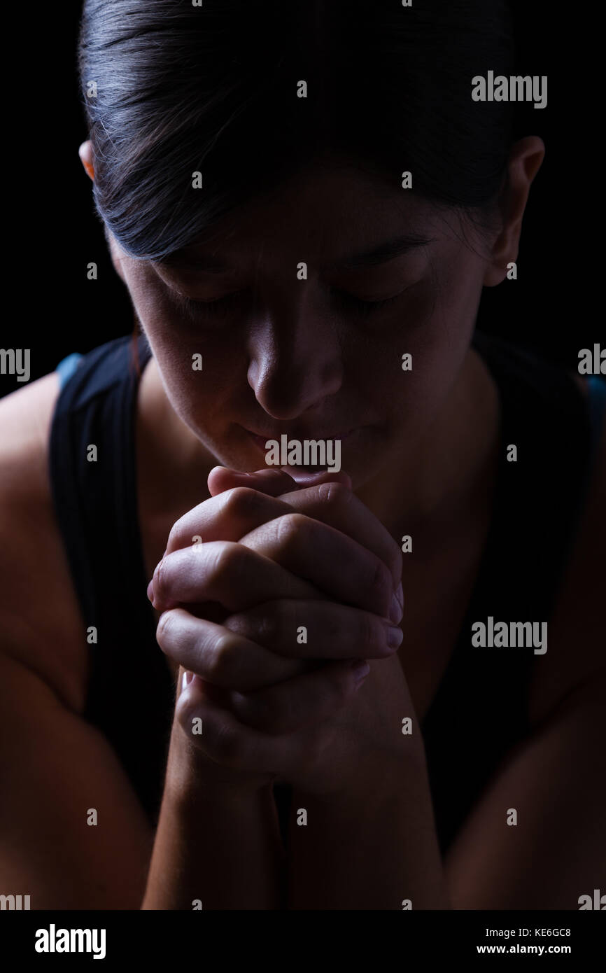 Low Key Porträt einer gläubigen Frau zu beten, die Hände gefaltet in Gottesdienst, Kopf und Augen in religiöser Inbrunst geschlossen, auf einem schwarzen Hintergrund. Stockfoto