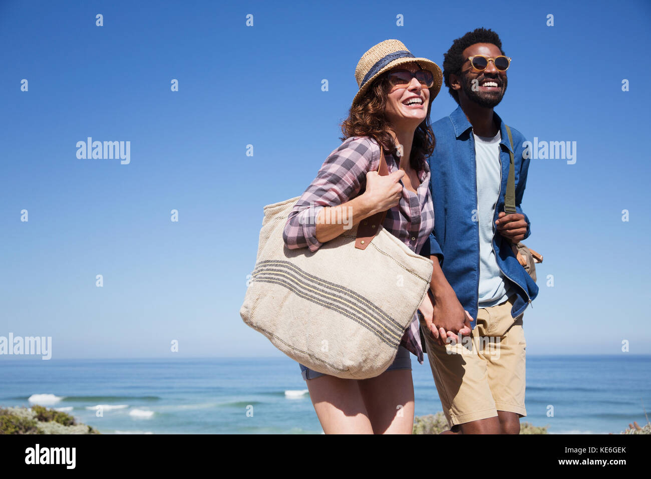 Lächelndes, liebevolles Paar, das sich an einem sonnigen Sommerstrand hält Stockfoto