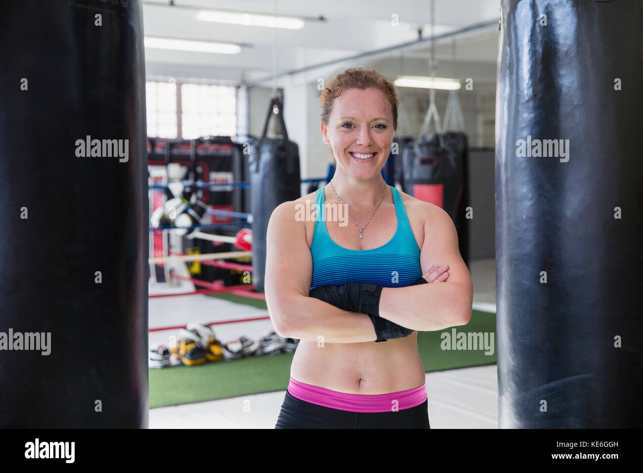 Portrait lächelnde, selbstbewusste Boxerin, die im Fitnessstudio bei Boxsäcken steht Stockfoto