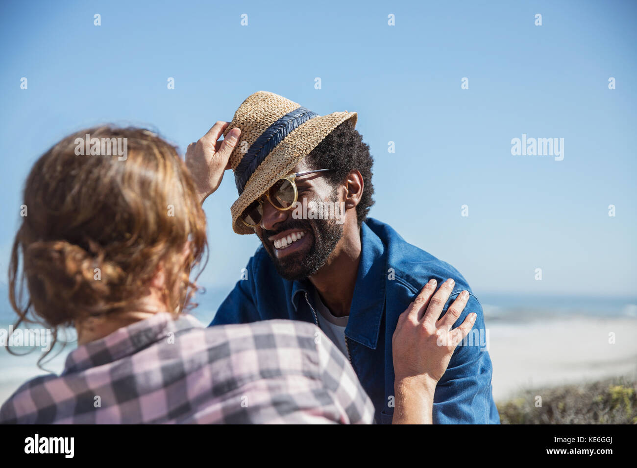 Verspieltes multiethnisches Paar mit Hut am sonnigen Sommerstrand Stockfoto