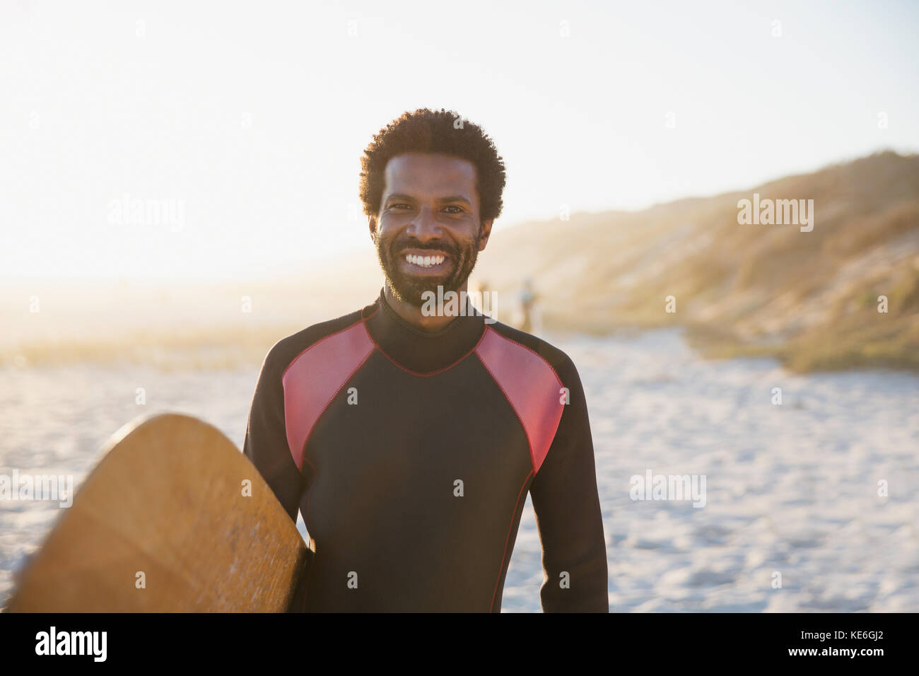 Portrait lächelnder, selbstbewusster Surfer mit Surfbrett am sonnigen Sommerstrand Stockfoto