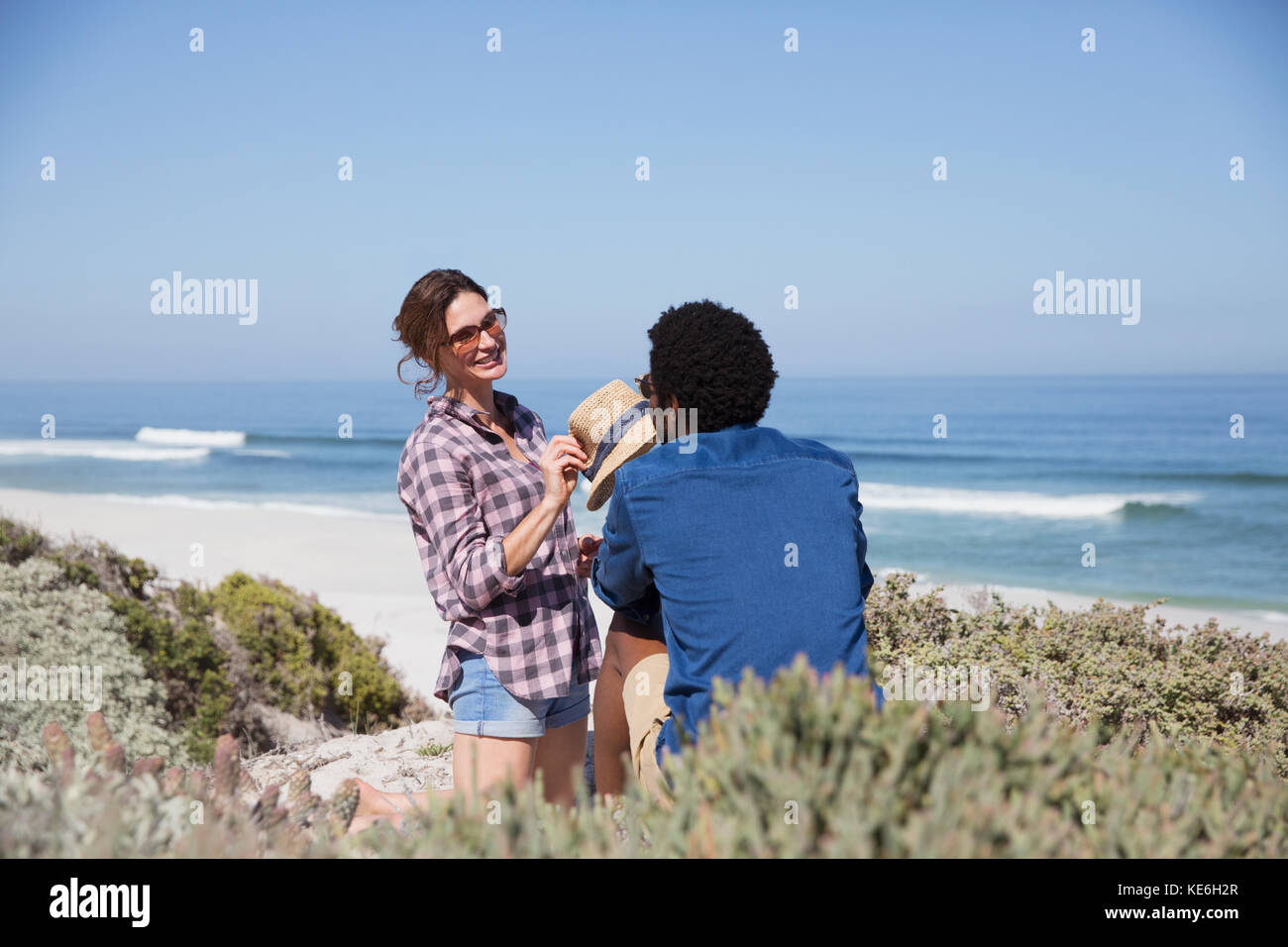 Lächelndes, multiethnisches Paar, das am sonnigen Sommerstrand spricht Stockfoto