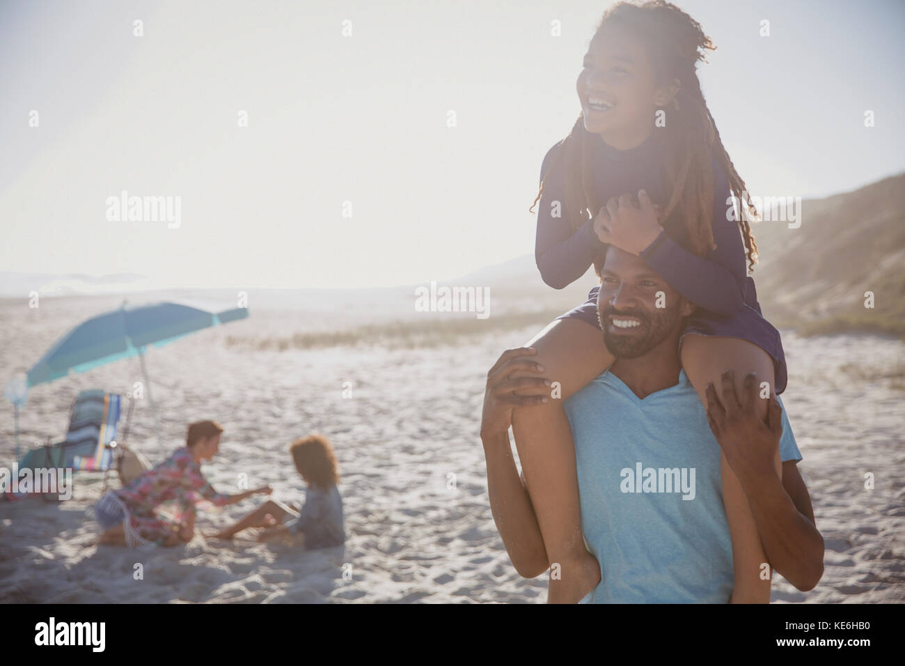 Lächelnder Vater trägt Tochter auf Schultern am sonnigen Sommerstrand Stockfoto