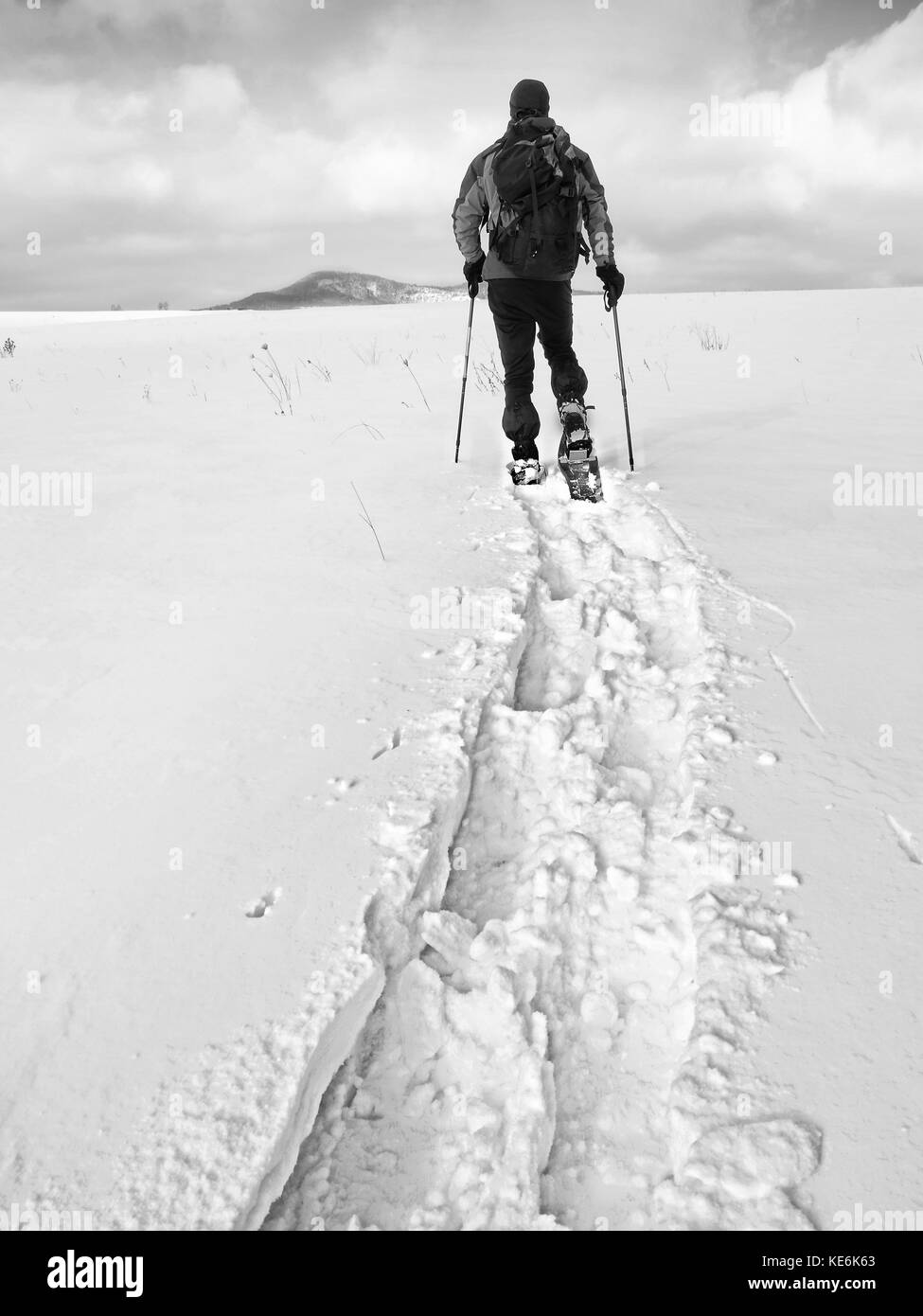 Wanderer mit Rucksack Schneeschuhwandern im tiefen Drift. Mann mit Schneeschuhen gehen im Hill. Wanderer in Grün Grau winter Jacke und schwarzen trekking Hose snowsho Stockfoto