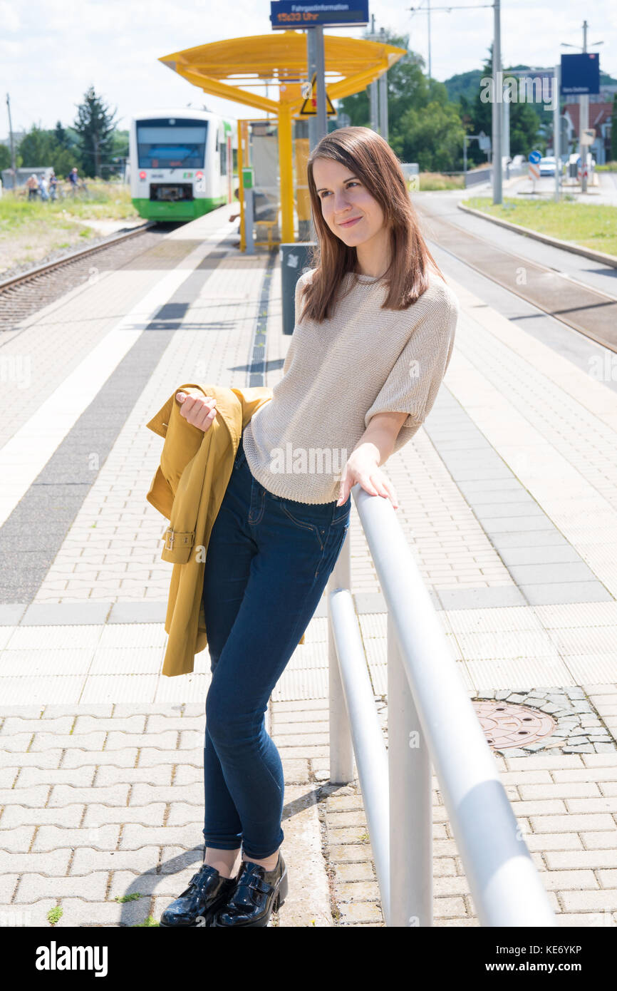 Junge Frau in einem gelben Regenmantel warten auf einen Zug auf einem Bahnhof Stockfoto