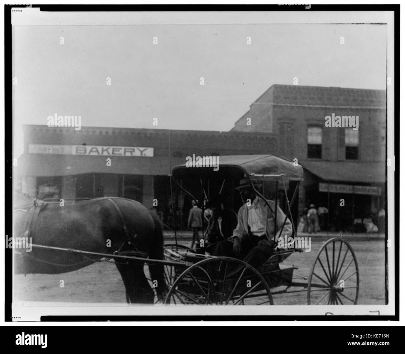 Zwei afrikanische amerikanische Männer im Pferd, Kutsche sitzend; Bäckerei und andere kommerzielle buildlings im Hintergrund LCCN 99472267 Stockfoto