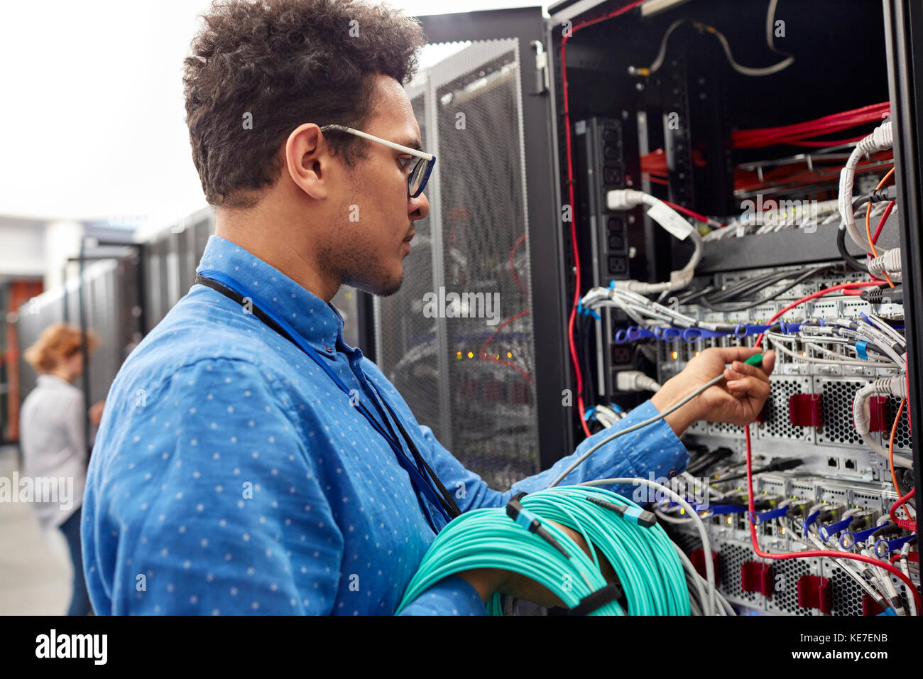 Männlicher IT-Techniker, der das Kabel in die Schalttafel im Serverraum einsteckt Stockfoto