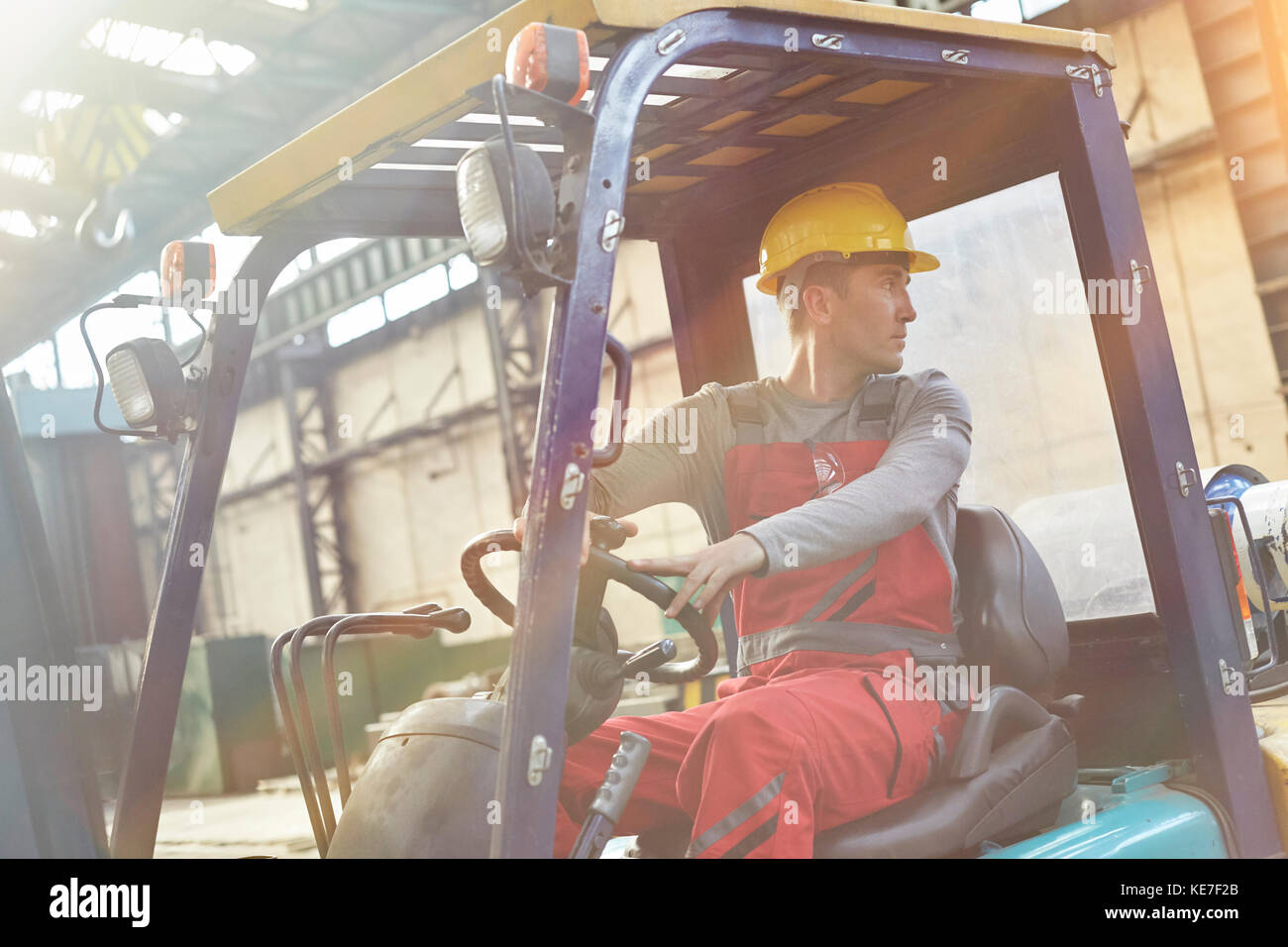 Männlicher Arbeiter, der Gabelstapler fährt und in der Fabrik wieder aufsteht Stockfoto
