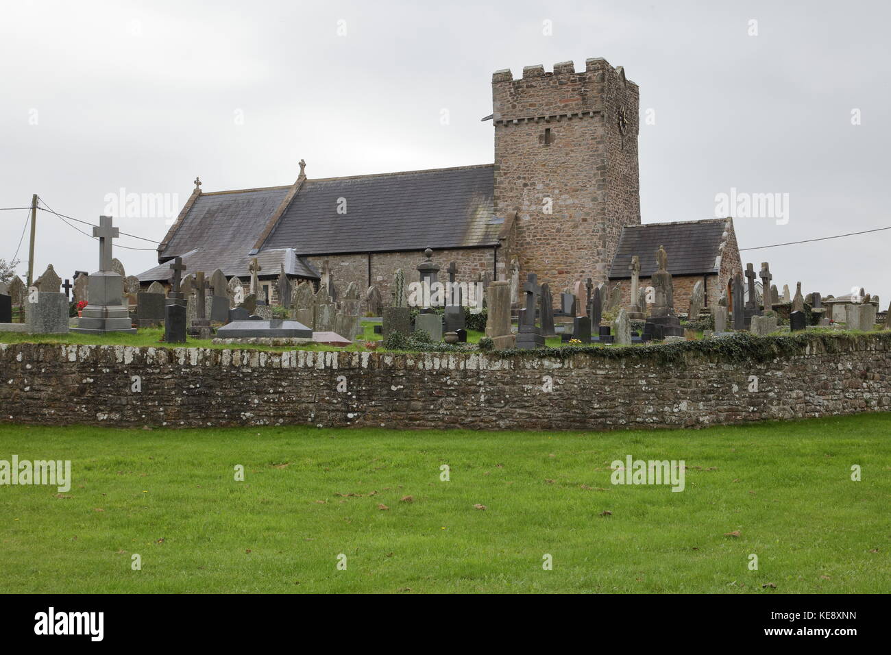 Einer ländlichen Kirche und Friedhof mit Viele Grundsteine innerhalb des ummauerten Friedhof an einem trüben Tag. Stockfoto