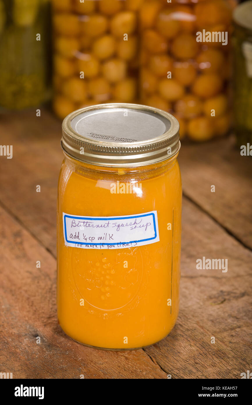 Glas homecanned butternut Kürbis Suppe, ruht auf einem rustikalen, mit Holz Tischplatte, mit anderen homecanned waren (rainier Kirschen und Pickles) im backgrou Stockfoto