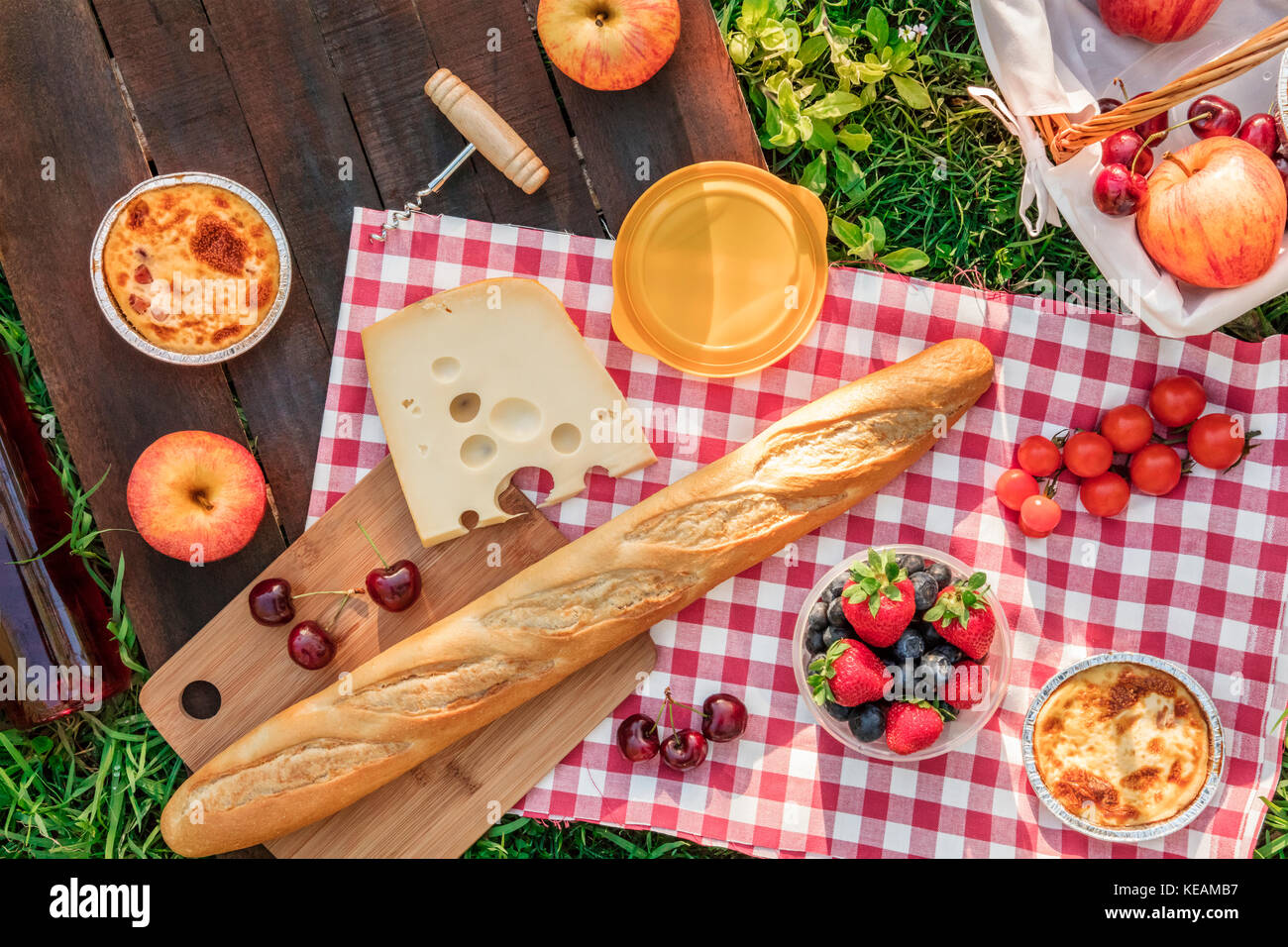 Ein Foto von einem Picknick mit einem Apple, eine Flasche rose Wein, frische Kirschen, eine Quiche, einen Korkenzieher und ein Stück Käse, auf einem rustikalen Holzmöbeln b Stockfoto