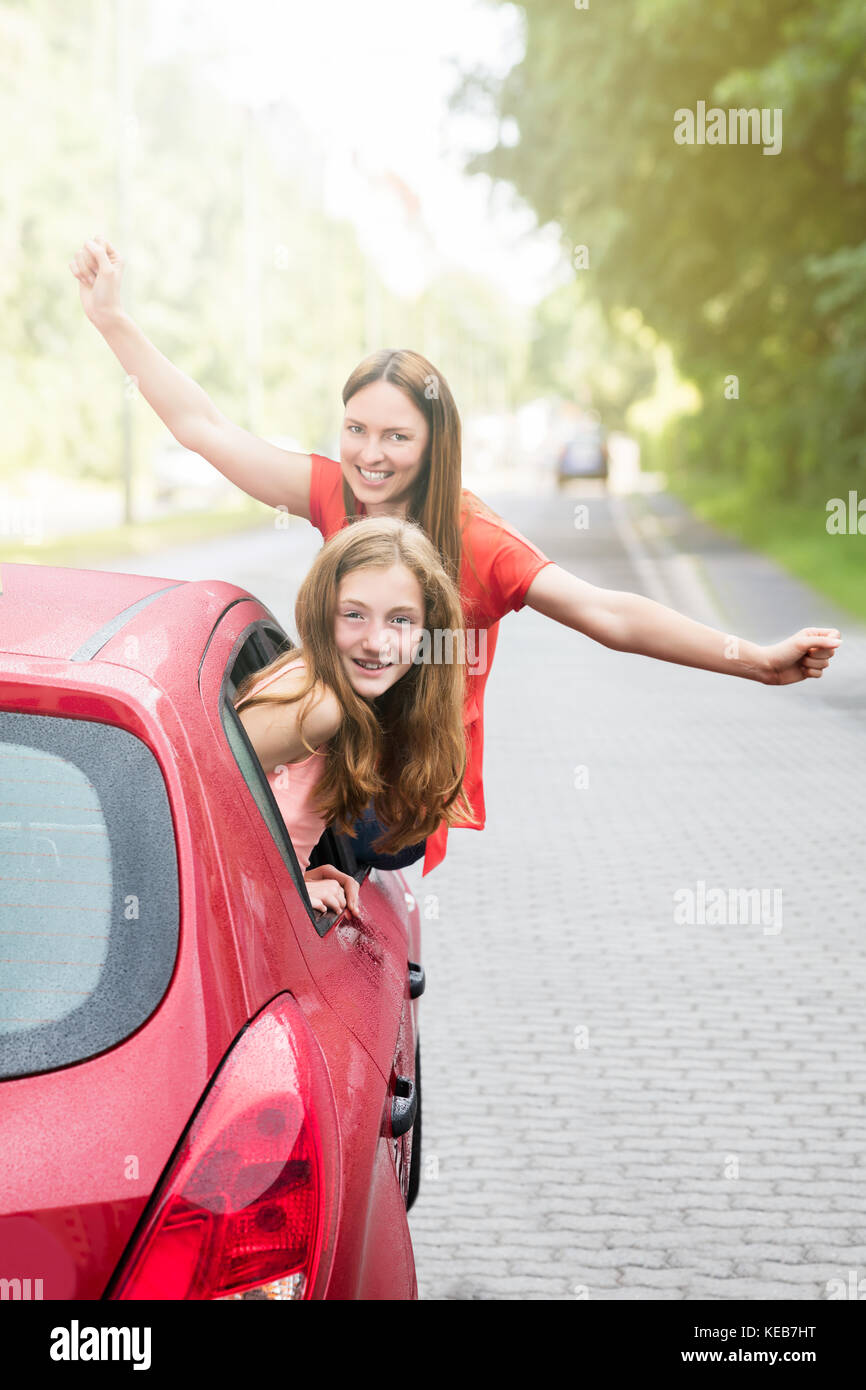 Glückliche Mutter und Tochter heben Ihre Arme beim Gehen für eine Fahrt im roten Auto Stockfoto