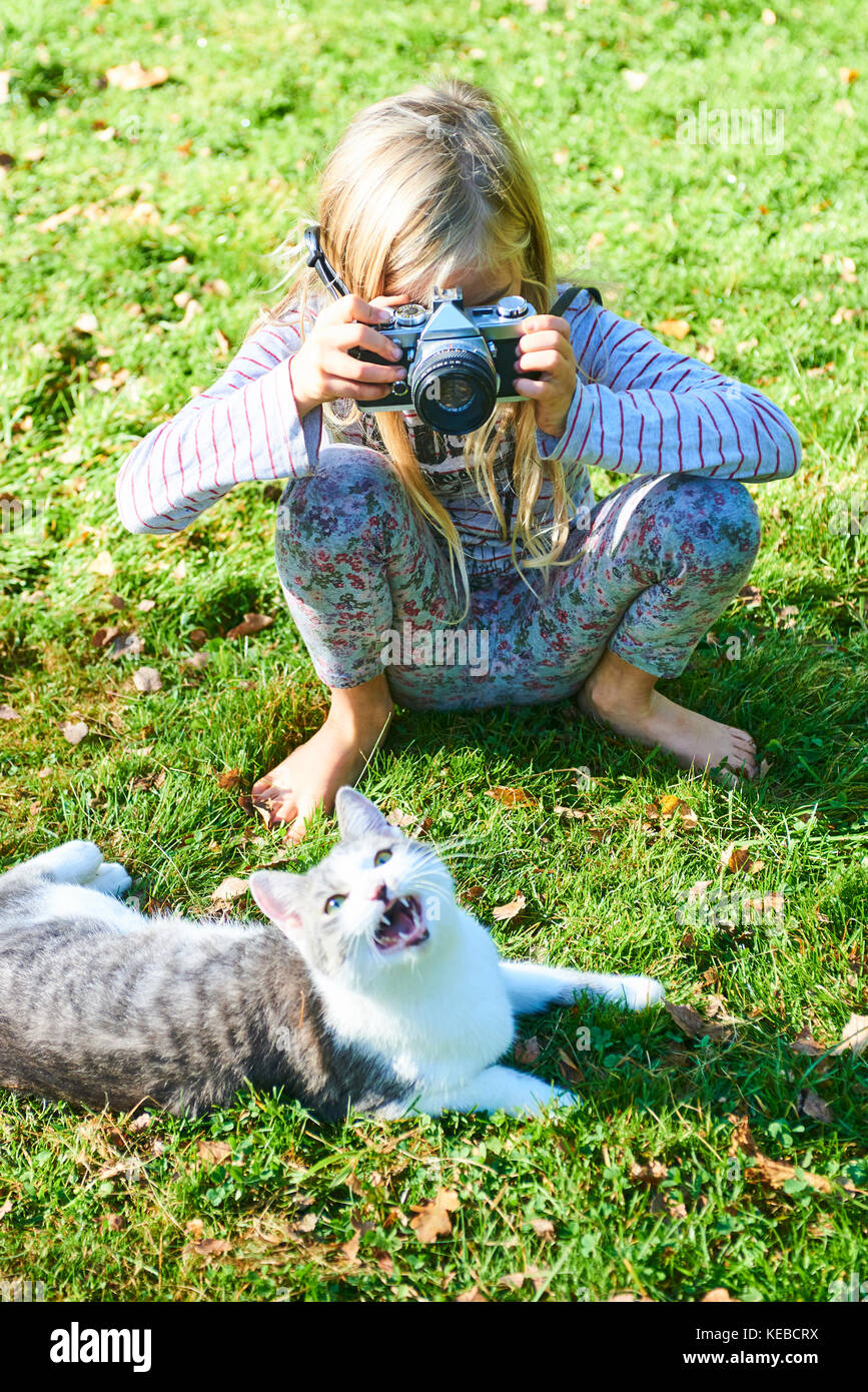 Kind Mädchen Fotografieren einer Katze, die auf dem Gras draussen im Garten. Stockfoto