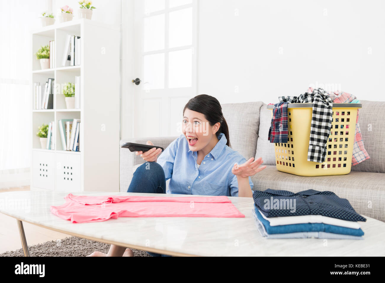 Schöne attraktive Frau, die allgemeine Ordnung und Sauberkeit Falten Kleidung und Fernsehen lustig Programm entspannen im Wohnzimmer. Stockfoto