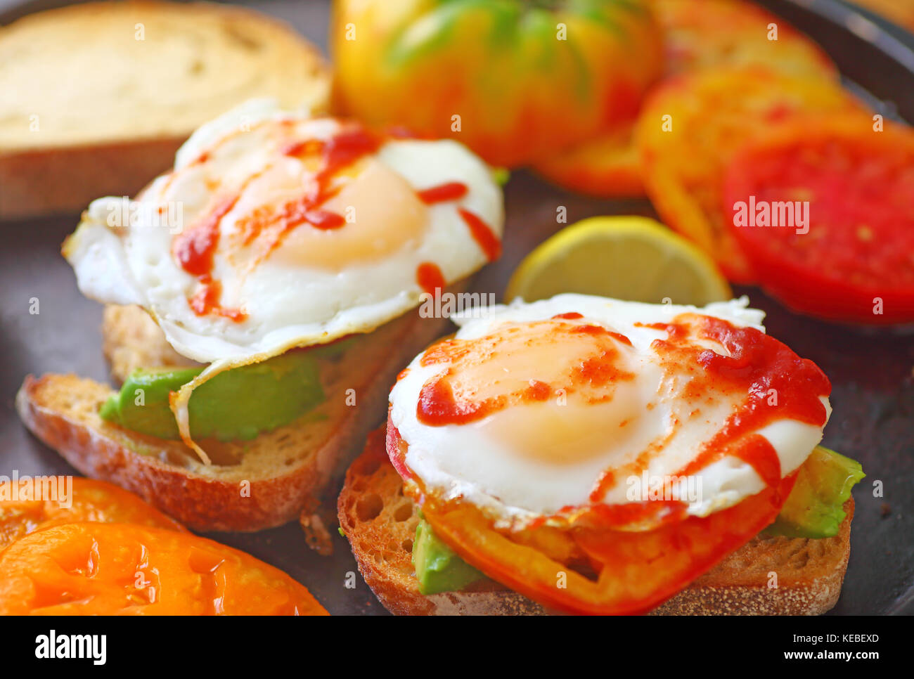 Aufgeschnittene Avocados auf Toast mit Spiegelei, heirloom Tomaten und Hot Chili Sauce Stockfoto