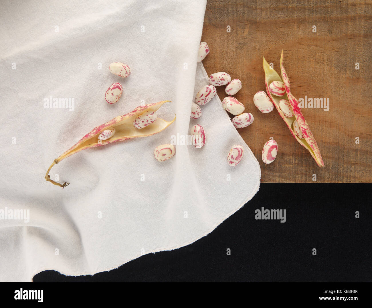 Die Gemeinkosten der Cranberry Beans, einige in der Shell, andere locker auf ein weißes Tuch auf einer Holzoberfläche mit Raum für Text Stockfoto