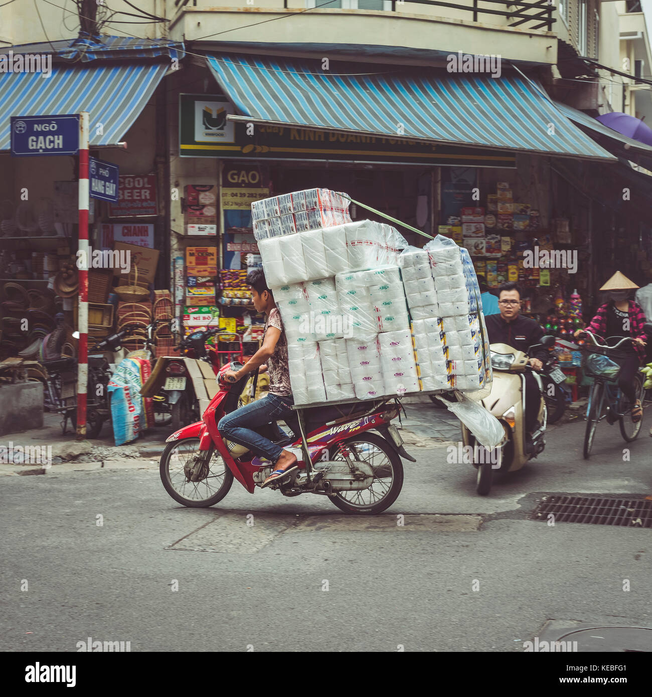 Ein Händler transportiert seine Waren auf einem Moped durch die belebten Straßen der Altstadt von Hanoi Quartal Stockfoto