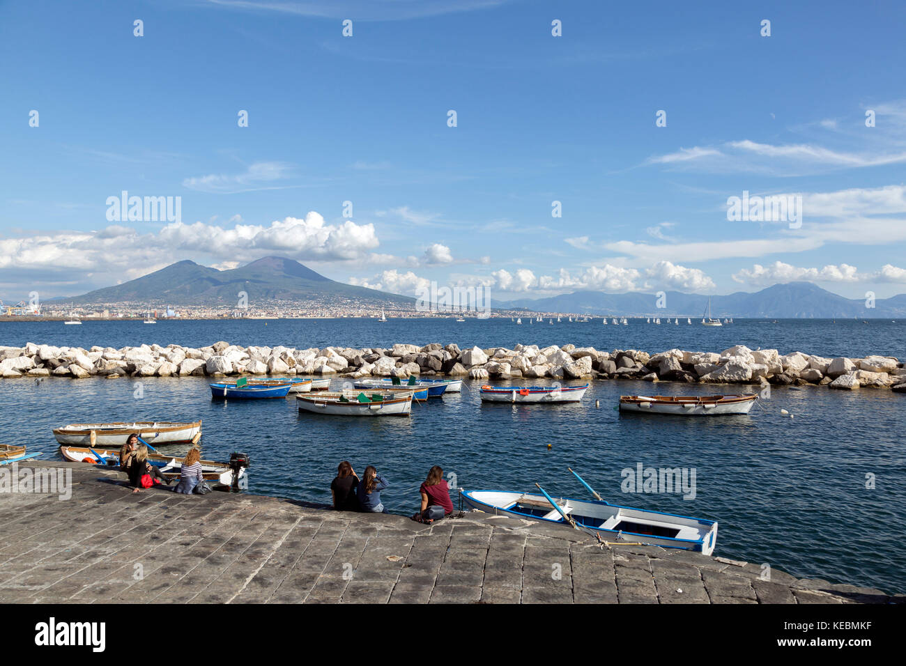 Szene an der Küste der Bucht von Neapel, mit Touristen, Fischerboote, felsigen Küste. Segelboote und Vesuv im Hintergrund Stockfoto