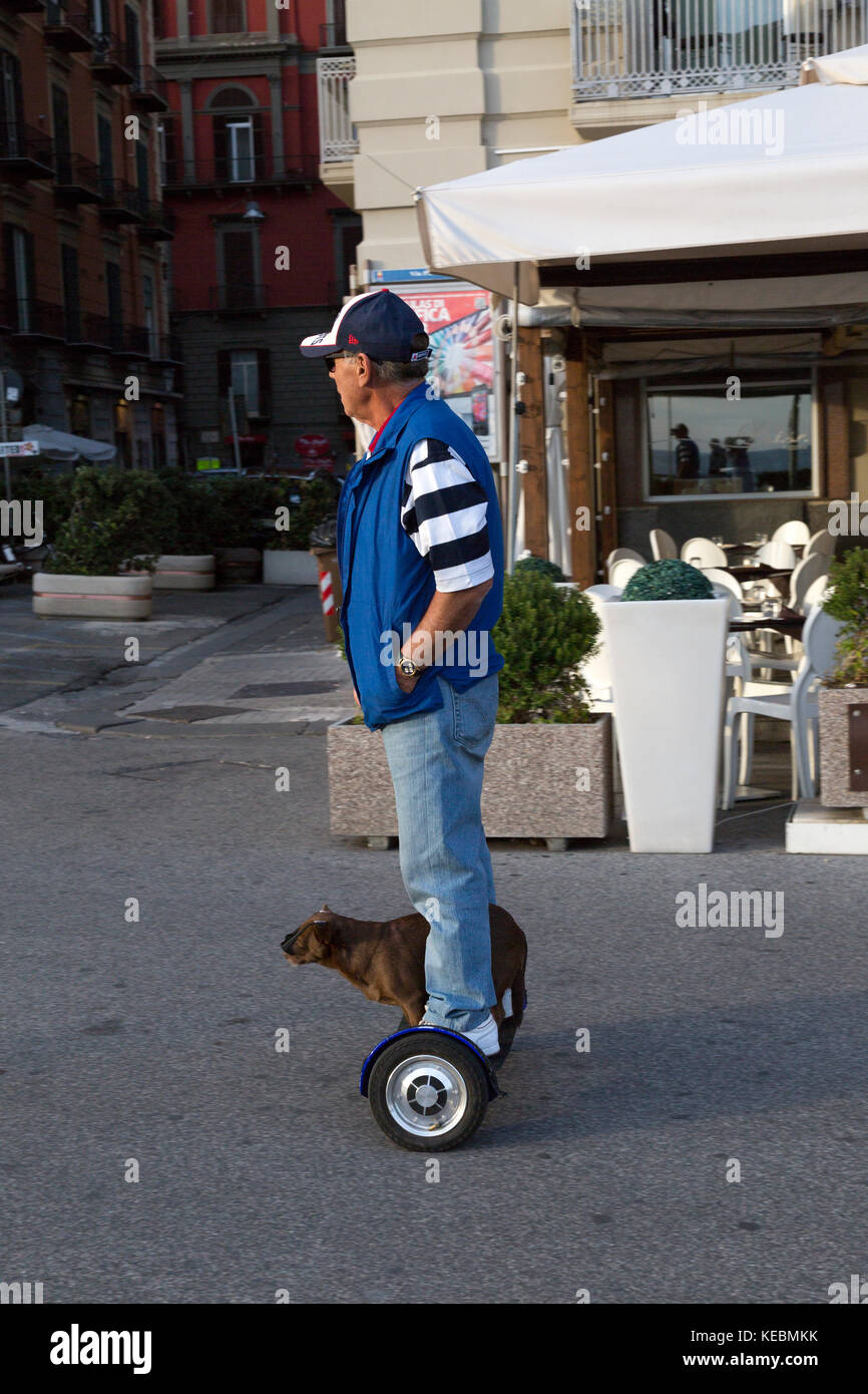 Mann mit Hund Reiten eine hover Board entlang der Straße in Neapel, Italien. Der Hund ist mit Sonnenbrille. Stockfoto