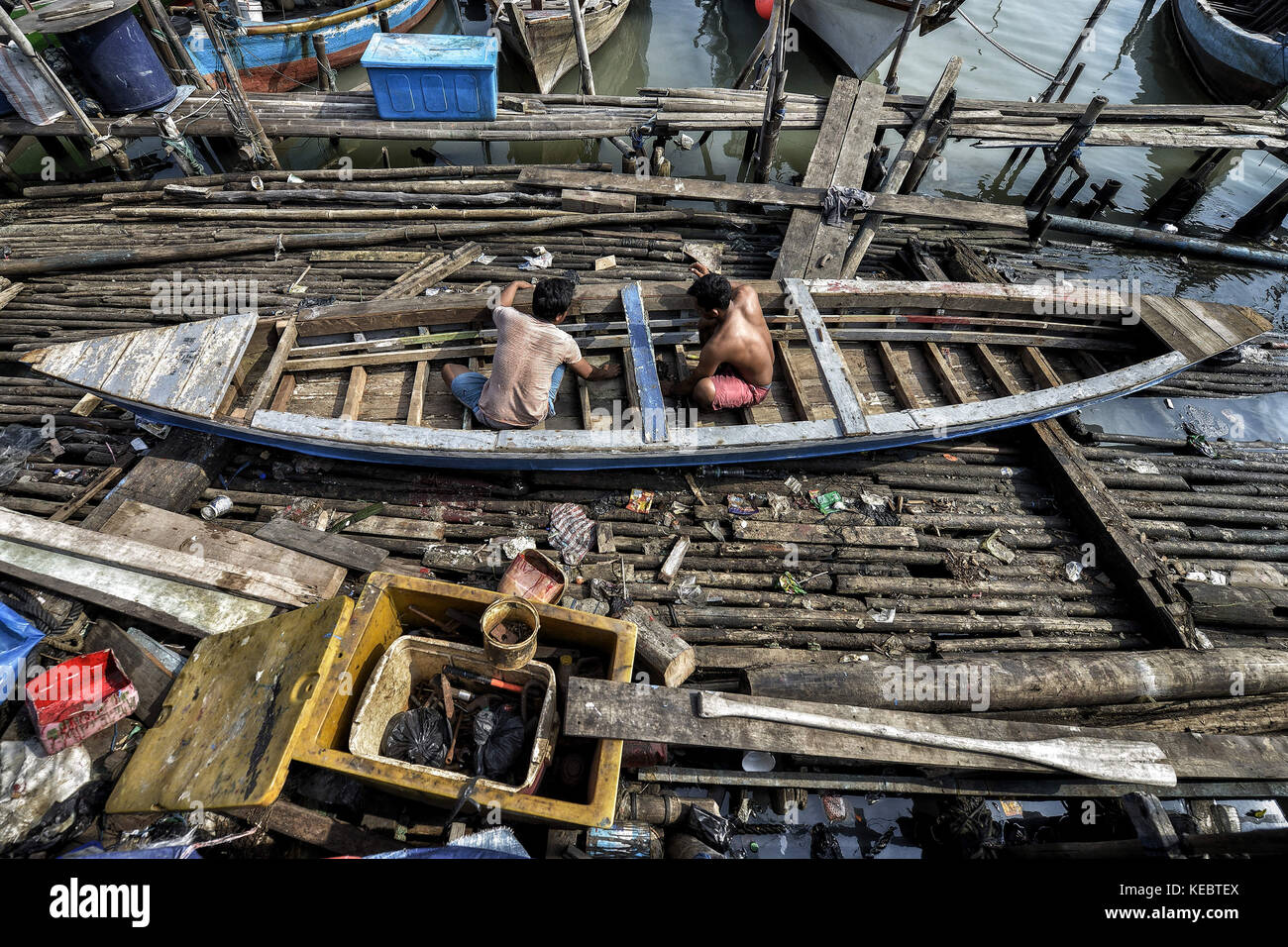 Jakarta, Java, Indonesien. August 2016. Zwei Männer werden gesehen, wie sie ein Fischerboot in der Pasar Ikan Nachbarschaft von Jakarta reparieren. Im April letzten Jahres stürmten Hunderte von Soldaten und Polizisten Pasar Ikan, ein historisches Fischerviertel nördlich von Jakarta, und machten alles in Trümmer. Wo es Backsteinhäuser gab, jetzt gibt es Berge von Schutt und Zelten. Die Einwohner zögern, die Nachbarschaft zu verlassen und weigern sich, in die von den Behörden gewährten Schutzhütten zu ziehen, weil sie behaupten, sie könnten sich diese nicht leisten. Es sind Vertreibungen ohne Vorankündigung oder Stockfoto