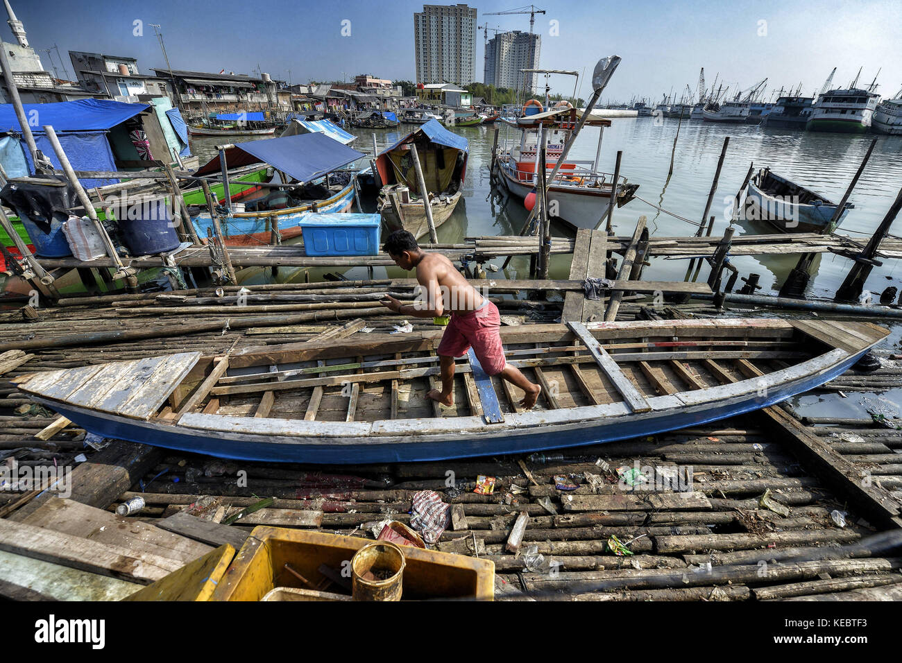 Jakarta, Java, Indonesien. August 2016. Ein Mann wird gesehen, wie er ein Fischerboot in der Pasar Ikan Nachbarschaft von Jakarta repariert. Im April letzten Jahres stürmten Hunderte von Soldaten und Polizisten Pasar Ikan, ein historisches Fischerviertel nördlich von Jakarta, und machten alles in Trümmer. Wo es Backsteinhäuser gab, jetzt gibt es Berge von Schutt und Zelten. Die Einwohner zögern, die Nachbarschaft zu verlassen und weigern sich, in die von den Behörden gewährten Schutzhütten zu ziehen, weil sie behaupten, sie könnten sich diese nicht leisten. Es sind Vertreibungen ohne Ankündigung oder ohne Rücksicht Stockfoto