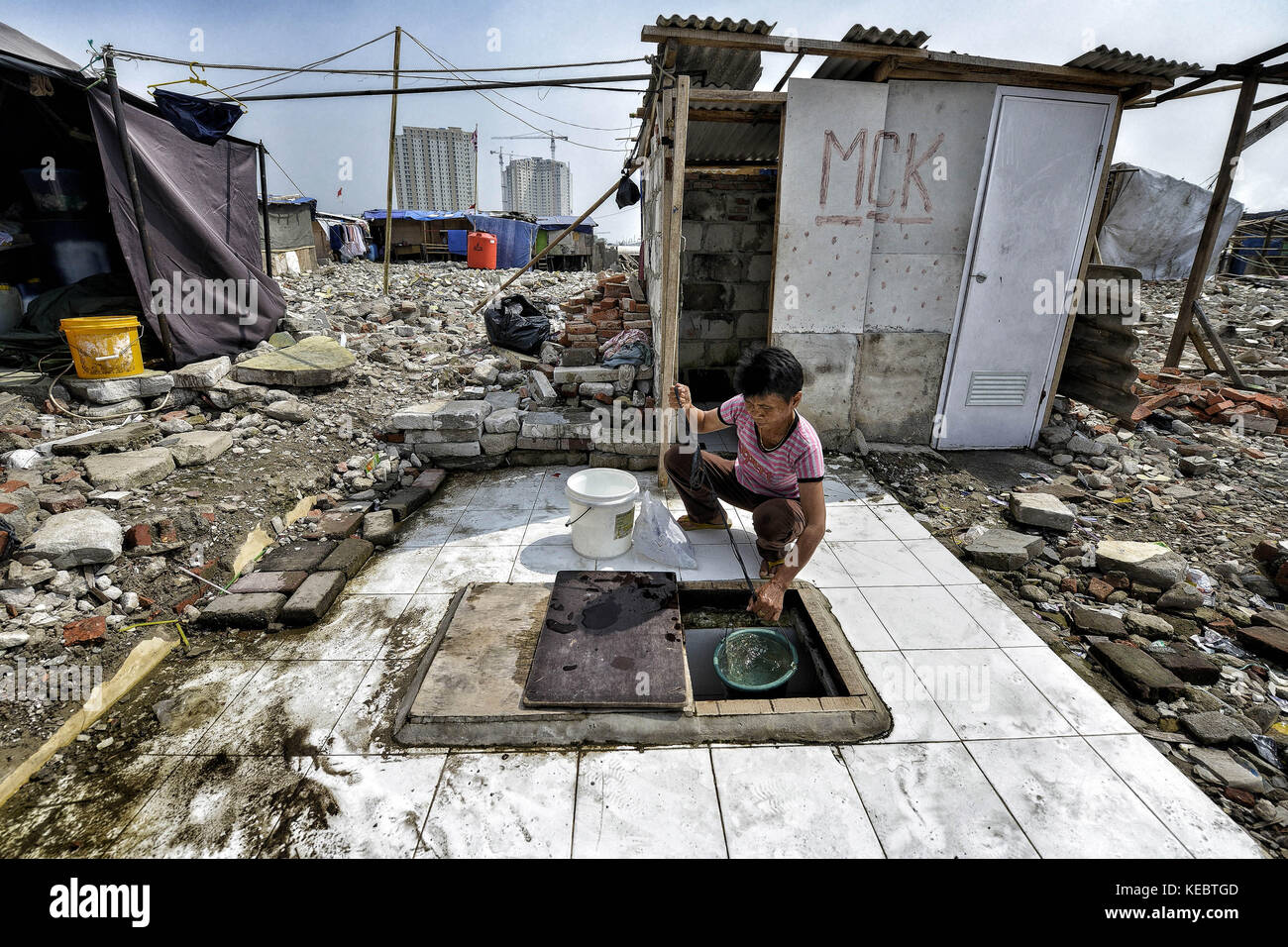 Jakarta, Java, Indonesien. August 2016. Eine Frau wird gesehen, wie sie Wasser aus einem Brunnen im Pasar Ikan Viertel von Jakarta nimmt. Im April letzten Jahres stürmten Hunderte von Soldaten und Polizisten Pasar Ikan, ein historisches Fischerviertel nördlich von Jakarta, und machten alles in Trümmer. Wo es Backsteinhäuser gab, jetzt gibt es Berge von Schutt und Zelten. Die Einwohner zögern, die Nachbarschaft zu verlassen und weigern sich, in die von den Behörden gewährten Schutzhütten zu ziehen, weil sie behaupten, sie könnten sich diese nicht leisten. Es handelt sich um Räumungen, die fast ohne Vorankündigung oder c Stockfoto