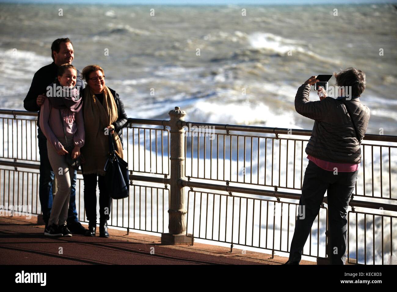 Hastings, East Sussex, UK. 20. Oktober 2017. Sonnig mit sehr stürmischen Bedingungen, Windgeschwindigkeit 25 km/h und Böen von bis zu 41 mph. Diese Touristen scheinen nicht in den Sinn, wie ein Mitglied der Familie ein Bild auf einem Mobiltelefon. Prognose für stürmisches Wetter für das Wochenende. Foto: Paul Lawrenson/Alamy leben Nachrichten Stockfoto