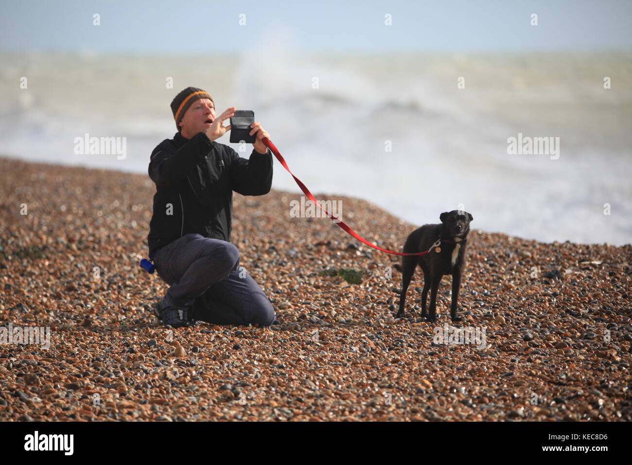 Hastings, East Sussex, UK. 20. Oktober 2017. Sonnig mit sehr stürmischen Bedingungen, Windgeschwindigkeit 25 km/h und Böen von bis zu 41 mph. Dieser Mann und seinem Hund einen Moment für ein Bild, während die Meere rage im Hintergrund. Prognose für stürmisches Wetter für das Wochenende. Foto: Paul Lawrenson/Alamy leben Nachrichten Stockfoto