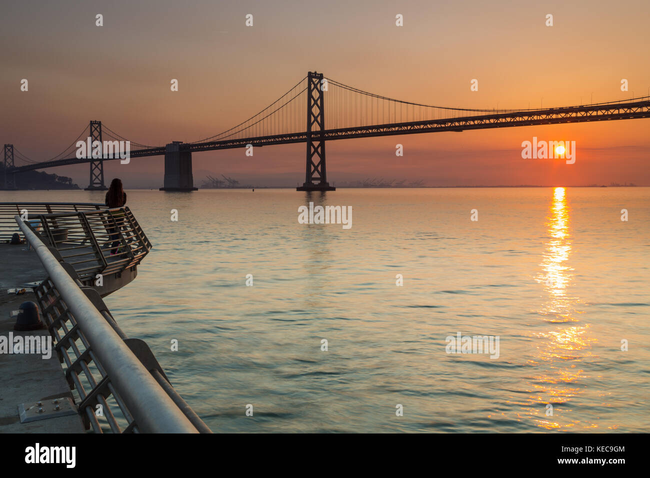 Eine Frau Uhren Sonnenaufgang über die Bay Bridge von Pier 14 in San Francisco. Stockfoto