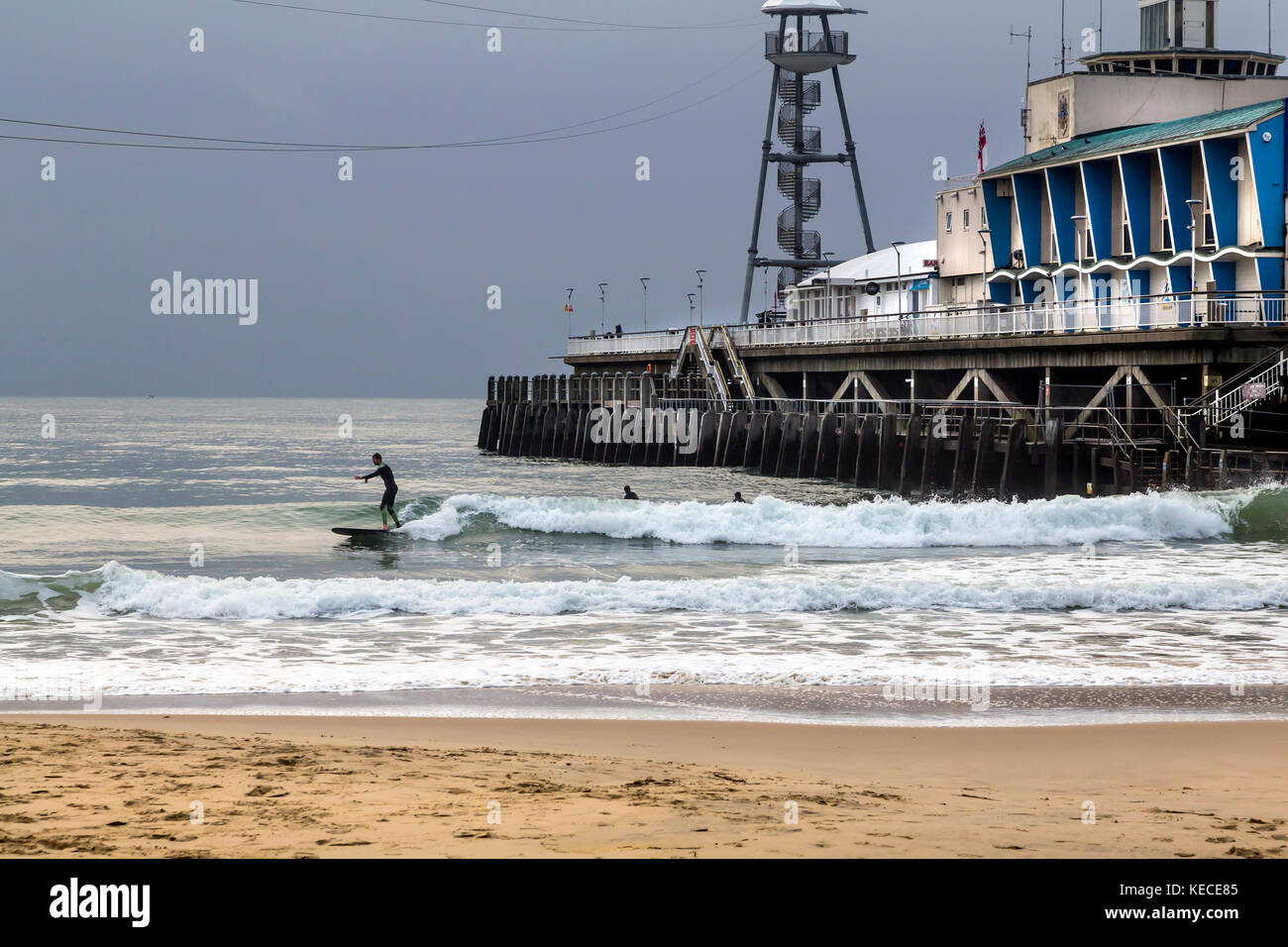 Surfen in der Nähe des Bournemouth Pier mit der aufgehenden Sonne wirft einen gelben Schein AUF DEM WASSER Stockfoto