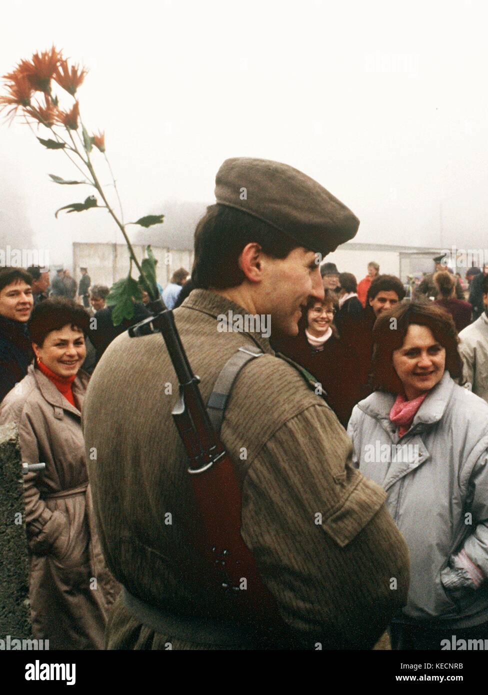 Am 10. November 1989 spricht und lächelt ein DDR-Grenzwächter mit einer Blume im Gewehrlauf am Ostpreußendamm in Berlin. Unter dem Druck der Bevölkerung öffnete die DDR am 9. November 1989 ihre Grenzen. Nach 28 Jahren macht die Berliner Mauer keinen Sinn mehr. | Nutzung weltweit Stockfoto