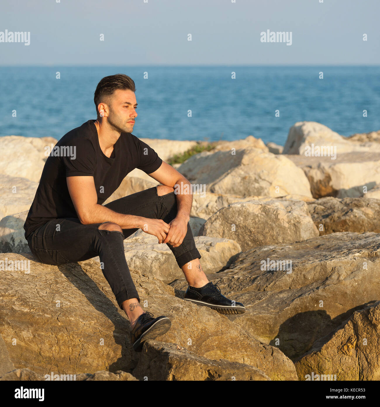 Porträt einer schönen jungen Mann sitzt auf den Felsen in der Nähe des Meeres. Stockfoto