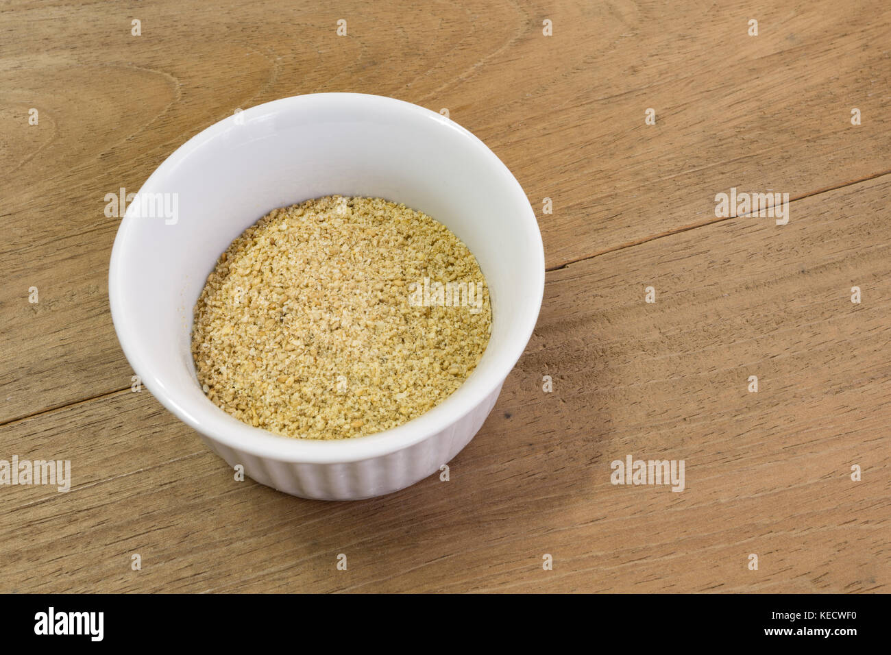 Boden geröstete Sesamsamen in weißer Keramik Schüssel, ramekin, Mitte links, auf hölzernen Tisch Stockfoto