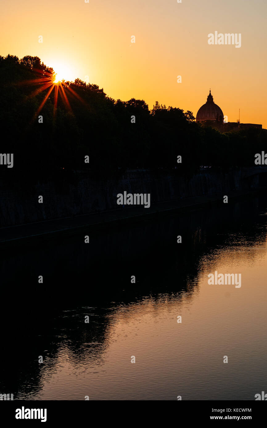 Ein helles orange Sonnenuntergang und Reflexion auf dem Tiber, Rom, mit der Kuppel von St. Peter Basilika im Hintergrund. Stockfoto