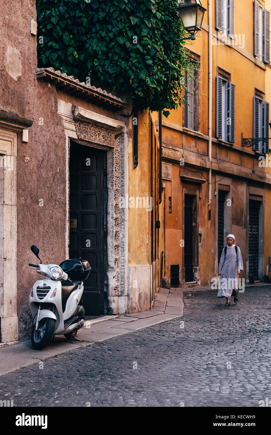 Eine Nonne geht der sonnenbeschienenen Straße in Richtung eines geparkten Roller in Rom, Italien, wo katholische Nonnen sind ein alltäglicher Anblick durch die Stadt Stockfoto