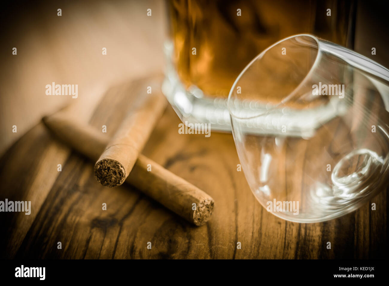 Nahaufnahme der beiden Zigarren, ein Glas und eine Flasche Rum auf einer hölzernen Oberfläche Stockfoto
