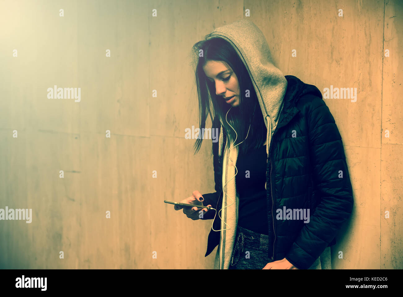 Eine schöne junge Frau in einem dunklen Stimmung Musik auf Ihr Smartphone in einem städtischen Umfeld. Stockfoto