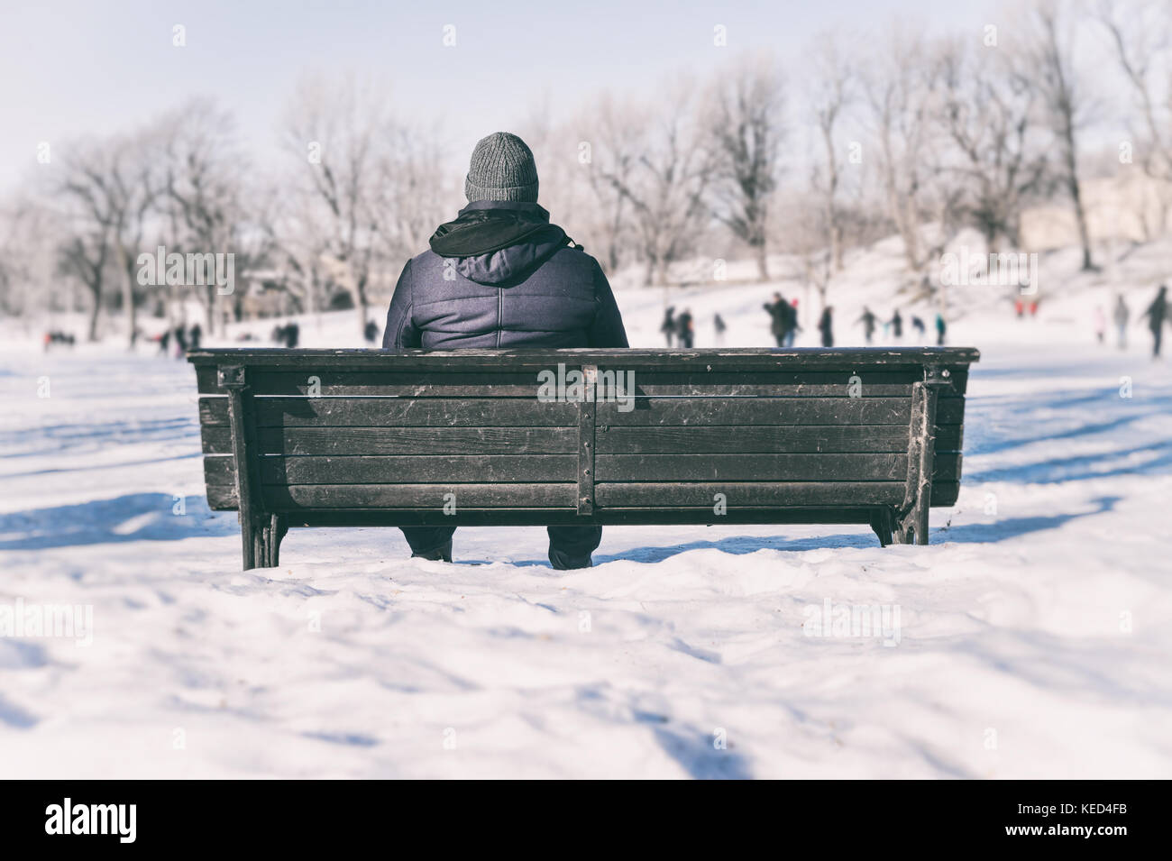 Mann sitzt auf der Bank mit Blick auf Leute Eislaufen Stockfoto