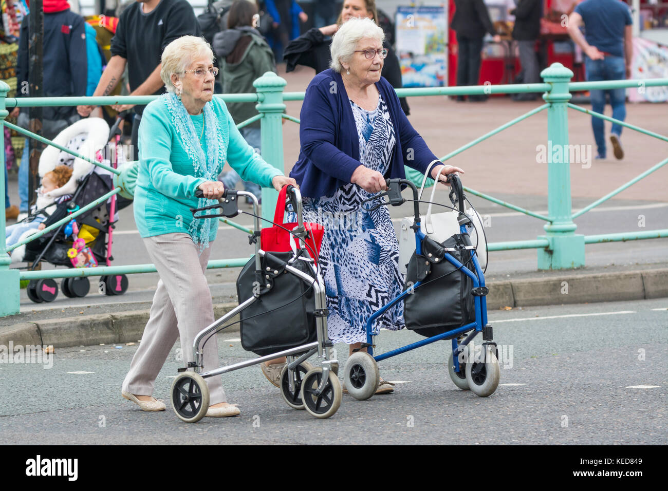Ältere Frauen überqueren eine Straße mit Wanderern auf Rädern in Brighton, East Sussex, England, Großbritannien. Zimmer Rahmen. Rollator. Jeden Tag. Stockfoto