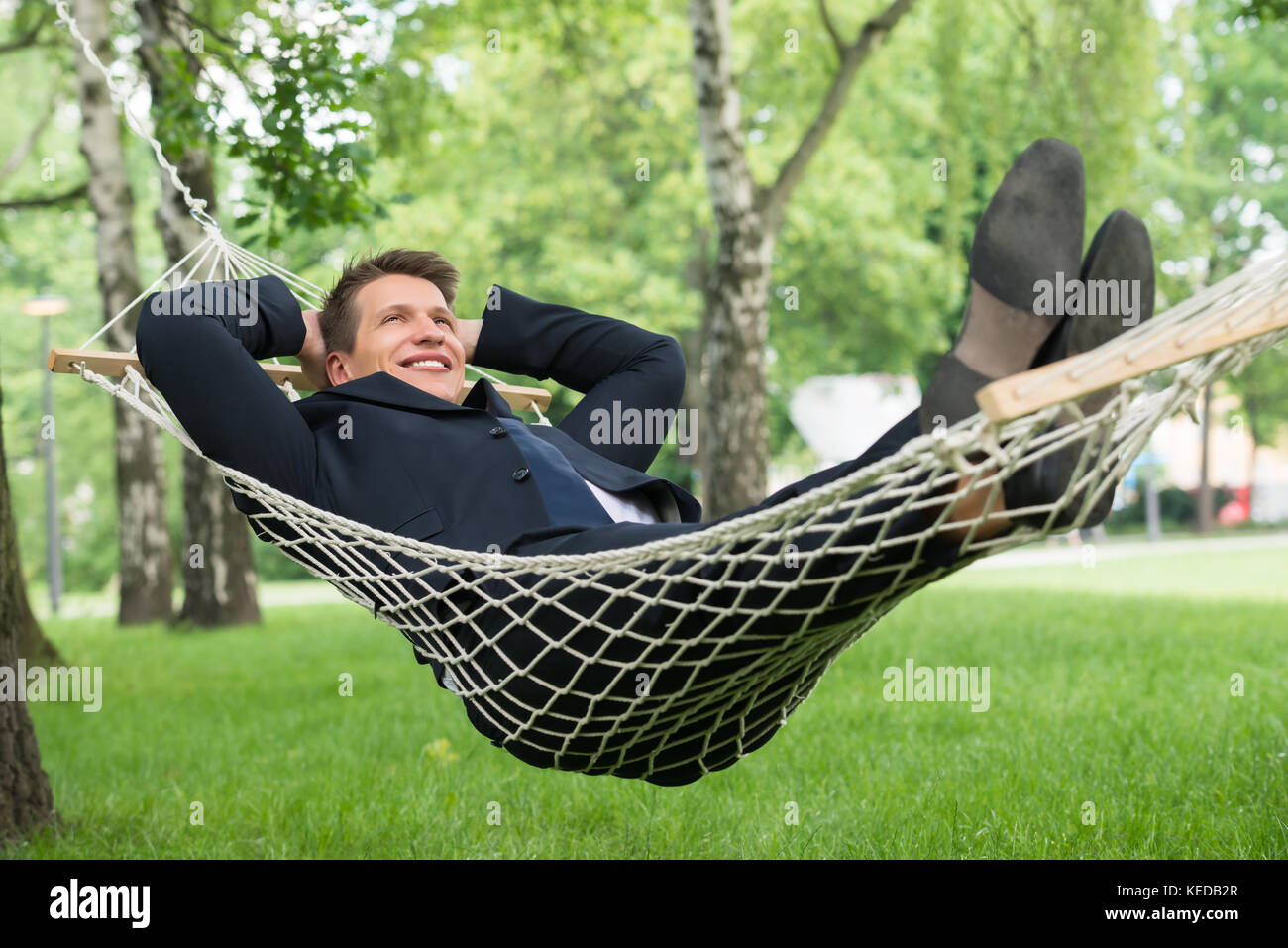Glückliche junge Geschäftsmann liegen in der Hängematte im Park Stockfoto