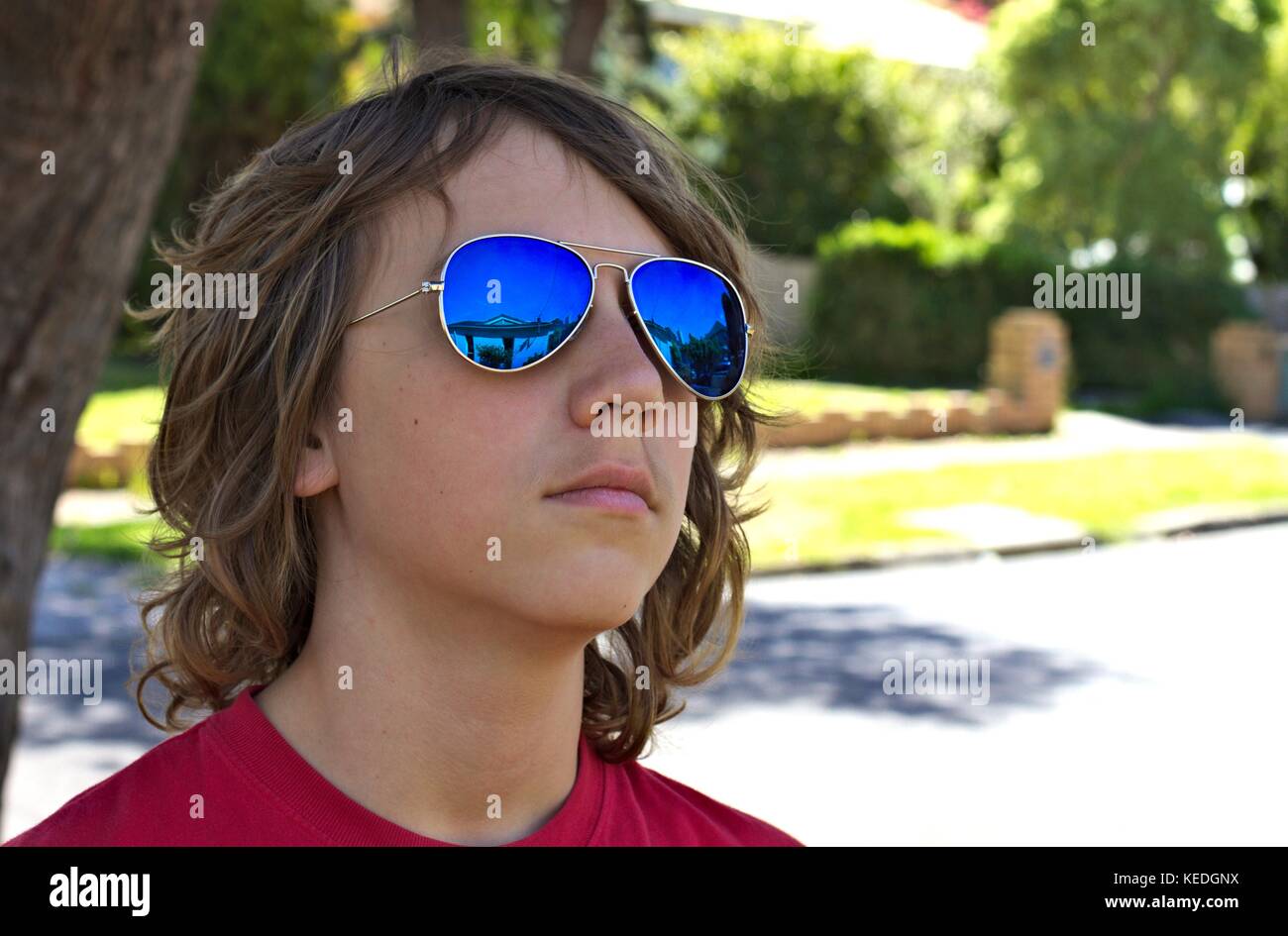 Junge Teenager männlichen trägt blaue Sonnenbrille Kopf gegen suburban Hintergrund gedreht. Stockfoto