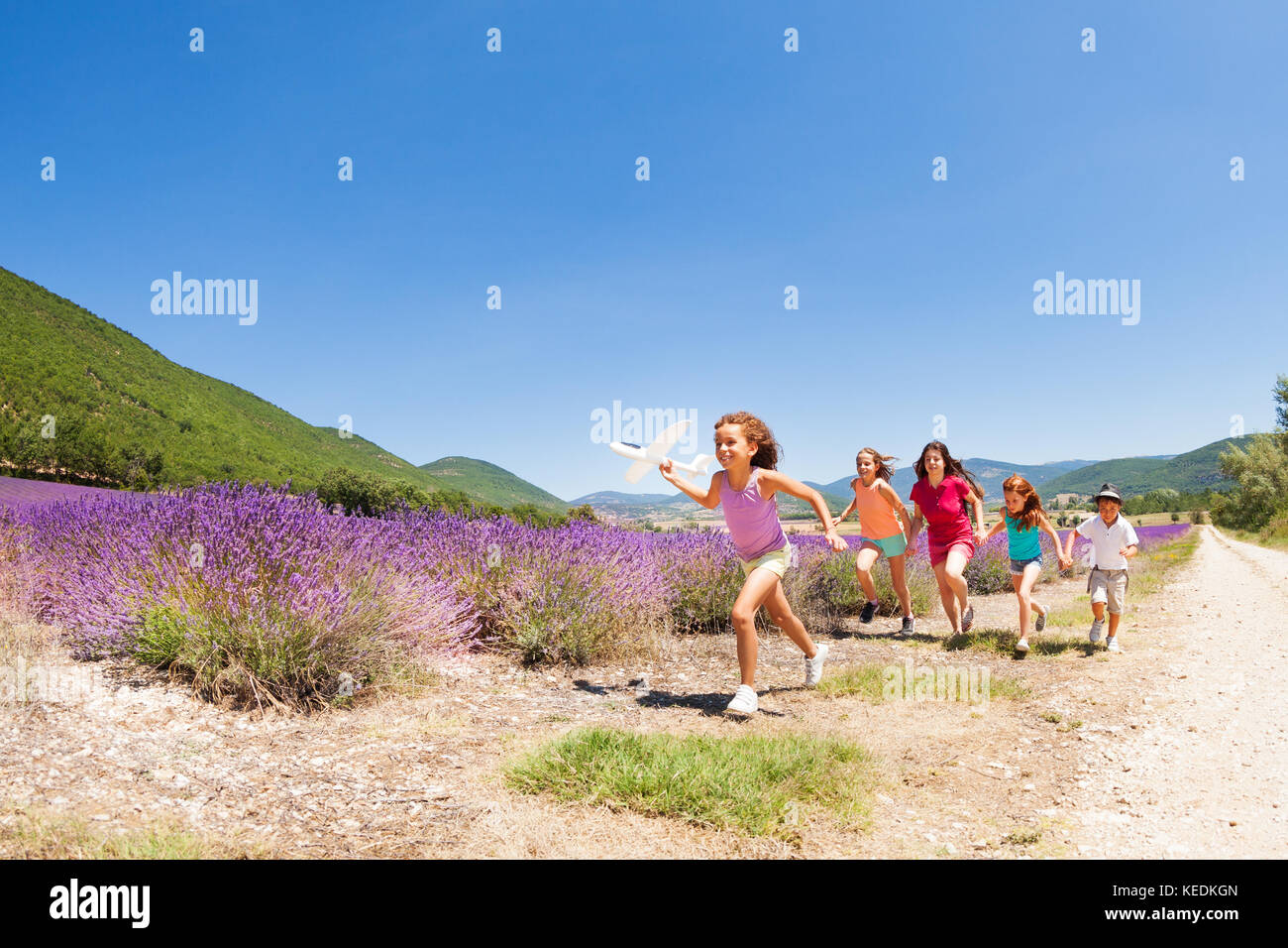Große Gruppe der glückliche Zeit - verschiedene Kinder mit Spielzeug Flugzeug durch Lavendelfeld in der Provence Stockfoto