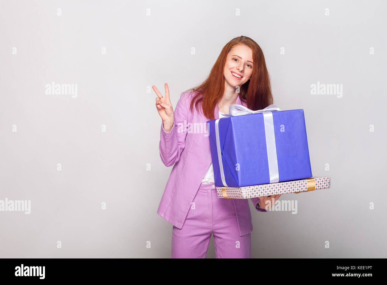 Ingwer schöne Mädchen, dass Geschenke Box und haben eine glücklich aus und zeigt ein v-Zeichen an Kamera. studio Shot Stockfoto