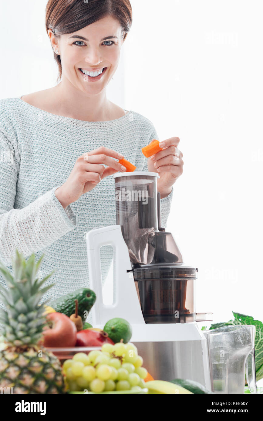 Junge lächelnde Frau mit einem Entsafter und eine gesunde vegane Drink mit frischen Karotten Stockfoto