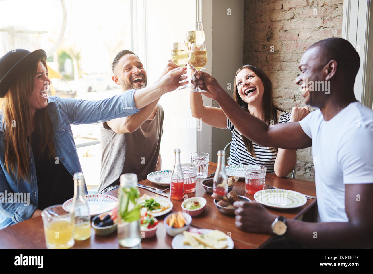 Gruppe von jungen Menschen versammelt, um gemeinsam zum Abendessen im Restaurant und klirren Gläser mit Wein und Lachen. Stockfoto