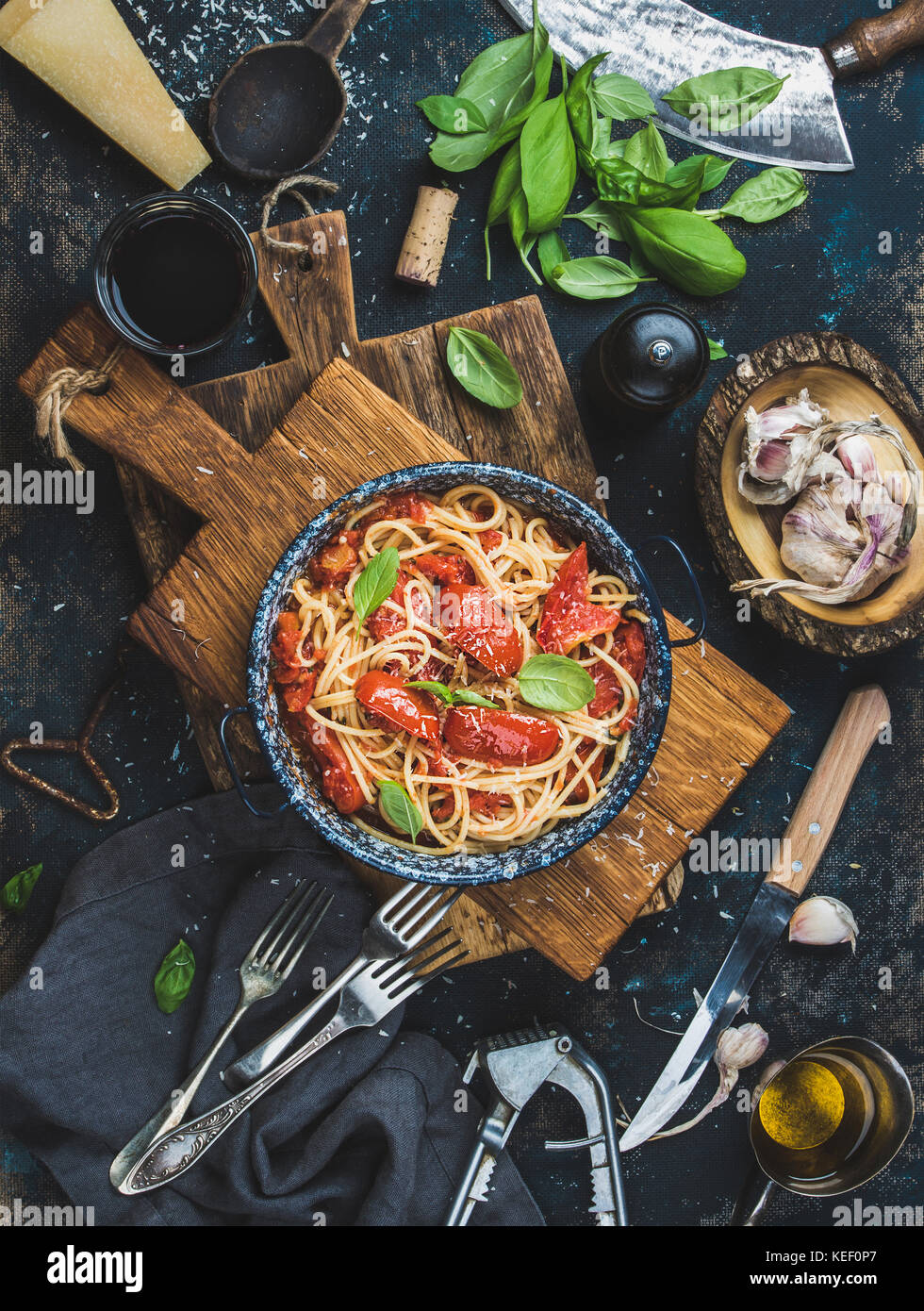 Italienisches Pastagericht. Spaghetti mit Tomaten und Basilikum in der Platte auf Holzbrett und Zutaten für das Kochen von Pasta über dunklen Sperrholz Hintergrund, t Stockfoto